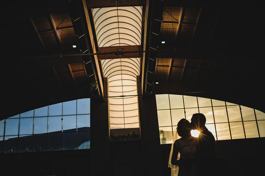 Silhouette of bride and groom kissing in an abandoned industrial ship at sunset