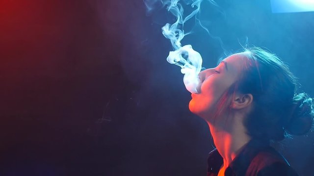 Young woman smokes electronic cigarette in color light. Night life and vape concept
