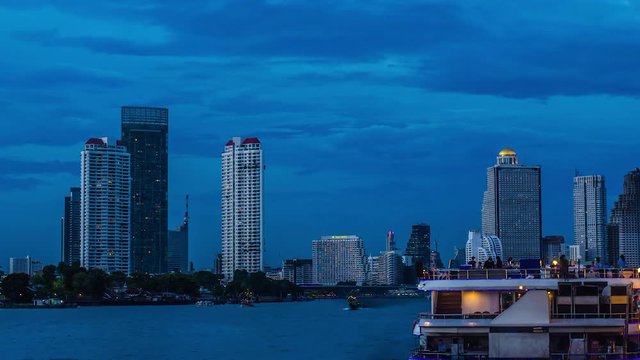 Timelapse - Bangkok city of High Rise Buildings at sunset with lighted boats on the river.