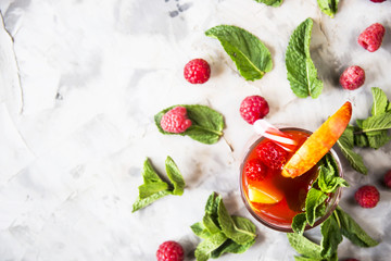 A light summer refreshing drink with fruits and berries - sangria next to mint leaves and raspberry berries on a gray background. Top view, flat lay