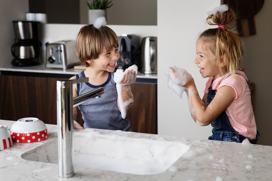 Laughing kids playing with suds while washing dishes