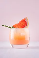 Tuinposter Cold detox cocktail of grapefruit juice with ice, rosemary, slices citrus on soft light pink and white background. © finepoints