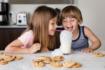 Laughing siblings making mess while blowing bubbles in glass of milk