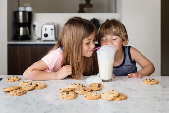 Naklejki Two kids blowing bubbles in glass of milk with straws