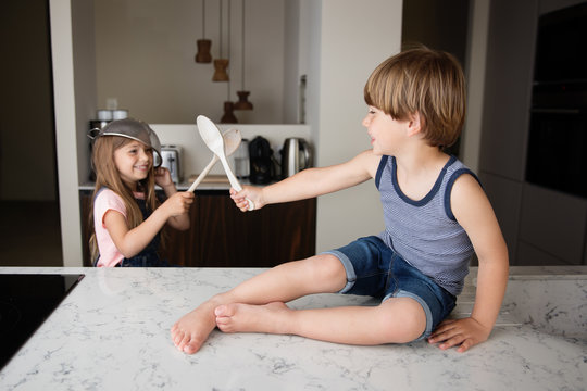 Siblings playing swords with wooden spoons in kitchen