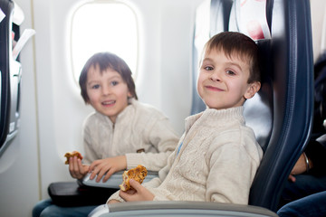 Two children, eating sandwiches on board in aricraft, traveling on vacation