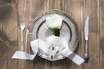Romantic table setting with white rose, vintage dishware, silverware on wooden table. Top view.