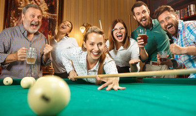 Young men and women playing billiards at office after work.