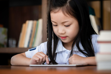 cute girl smile sitdown and playing laptop computer in the library, children concept, education concept