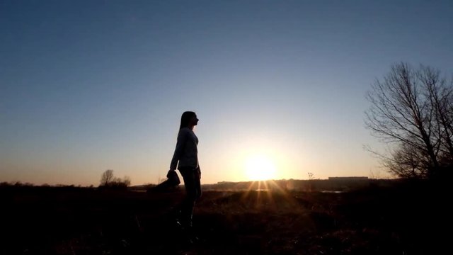 Silhouette of a young girl who is walk in field to take a pictures. Girl photographer with camera at the countryside at sunset time