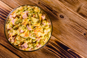 Salad with sausage, green pea, onion and carrot in glass bowl on wooden table. Top view
