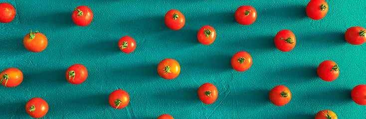 Red tomatoes cherry, scattered in a chaotic manner on a blue background. Food background. Panoramic banner