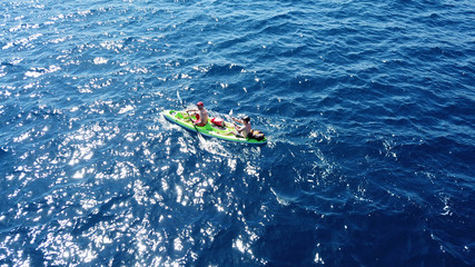 Aerial drone bird's eye view of sport kayak operated by 2 young men in deep blue open sea waters