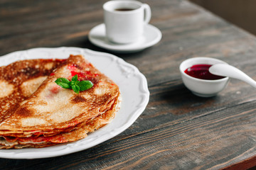 Traditional breakfast pancakes with jam on a plate on a wooden table close-up