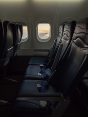 Empty three sites inside a flying airplane with wing and clouds view from window