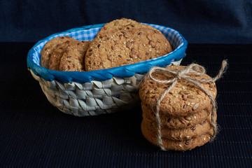 homemade oat cookies with sunflower seeds in and near blue checkered basket on black background