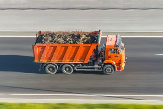 Truck dump with a load of soil in the body rides at high speed on the highway.