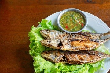 Fried mackerel and lettuce in dish on wooden table, Thai food style. copy space.