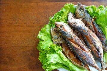Fried mackerel and lettuce in dish on wooden table, Thai food style. copy space.