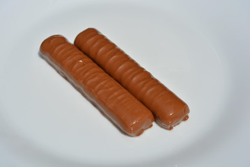 On a white plate of glass are two chocolate bars with a sandy liver and caramel, covered with a layer of milk chocolate