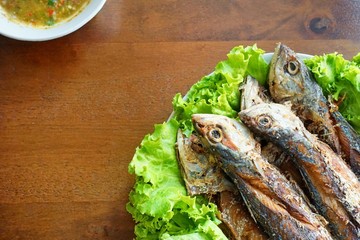 Fried mackerel and lettuce in dish on wooden table, Thai food style. copy space.