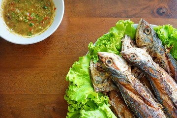 Fried mackerel and lettuce in dish on wooden table, Thai food style. copy space.