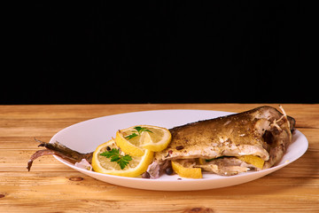 delicious roasted carp fish with lemon slices, spices, and fresh rosemary on white plate, view from above, close-up
