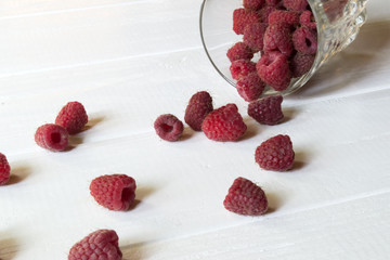Ripe raspberry in a glass, on a white wooden table.