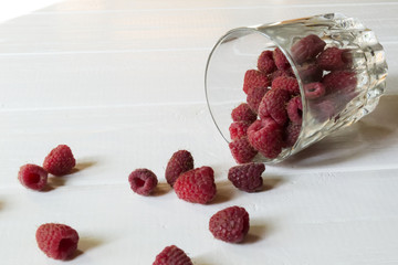 Ripe raspberry in a glass, on a white wooden table.