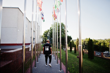 Stylish arabian muslim boy with originally hair posed on streets, against flags of different countries.