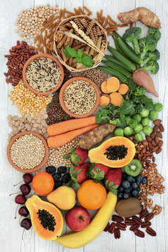 Healthy high fibre food with grains, legumes, whole wheat pasta, fresh fruit, vegetables, nuts, seeds and cereals. Top view on rustic background.