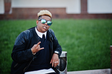 Stylish arabian muslim boy with originally hair and sunglasses posed on streets, sitting on bench.