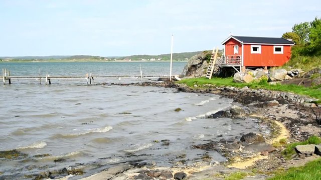 Red wooden cabin with a ladder leading up to the porch. It is a windy but sunny day at the coast. Location Rortangen outside Kungalv in Sweden.