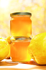 Quince jelly in glass jars with quinces on a wooden table in bright sunshine in front of an yellow and orange background
