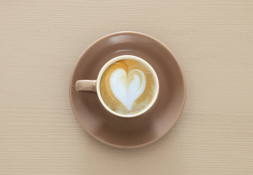 image of coffe cup with foam of heart shape over wooden table.