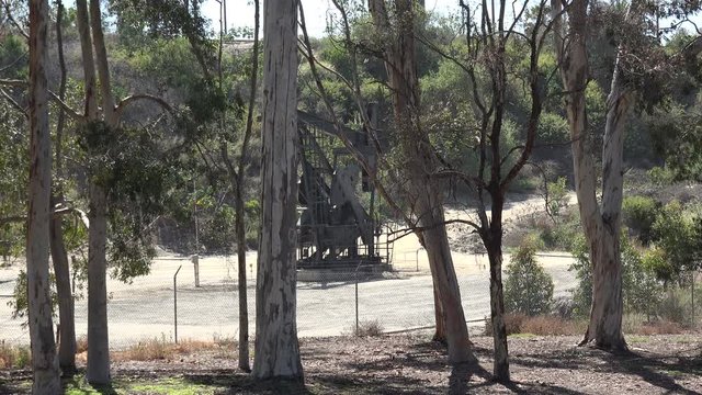 An oil pump jack seen through the trees of a forest

