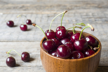 Juicy ripe cherries with sprigs in a wooden bowl on a rustic background