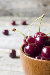 Juicy ripe cherries with sprigs in a wooden bowl on a rustic background