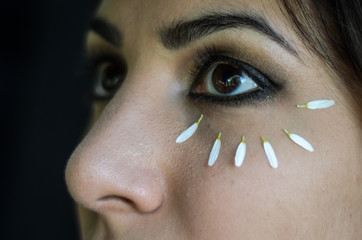Young charming girl doing eye make-up using petals of chamomile flowers