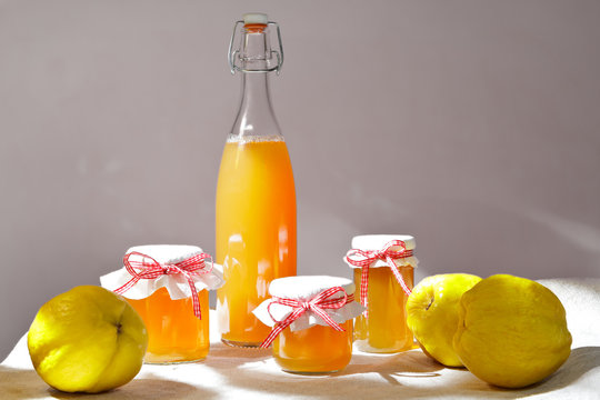 Homemade quince jelly and Juice in a bottle and glass jars with quinces on a linen tablecloth in bright sunshine in front of a neutral background.