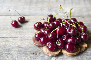 Juicy ripe cherries with twigs on wooden stand on rustic background