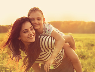 Happy enjoying loving mother hugging her playful laughing kid girl on sunset bright summer background. Closeup toned color bright portrait.