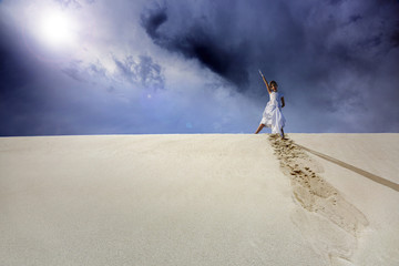 Młoda dziewczynka na szczycie piaszczystej wydmy, w białej sukience.