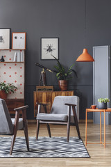 Living room interior with armchairs, orange lamp and coffee table, and wooden cabinets in the background on the grey wall