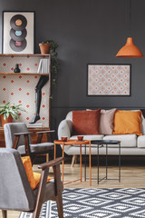 Retro living room interior with armchairs, sofa decorated with orange pillows, coffee table, poster, cupboard and patterned carpet