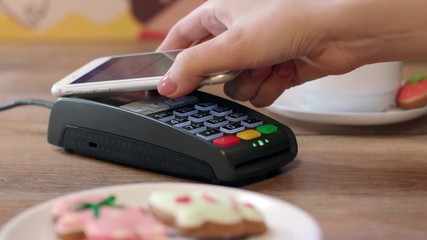 Mobile NFC payment for order in cafe. Hand of customer paying through mobile phone over pos terminal with NFC technology. Wireless money transfer through smartphone app. Apple pay concept