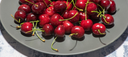 Dark, ripe and juicy cherries on a black plate