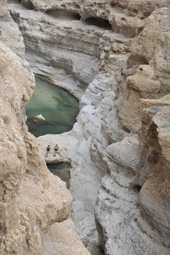 Sultanate of Oman, Wadi Shab, 2 persons are walking in a turquoise blue waters gorge surounded by limestone cliffs