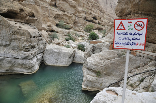 Sultanate of Oman, Wadi Shab, a sign written in arabic warn about the dangers of swimming in a gorge with turquoise blue waters
