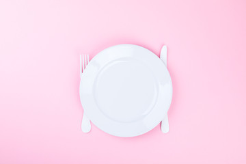 Concept minimal "Time to Eat". Fork, knife and white Plate on a pink pastel Background. Top View. Flat Lay. Copy space for Text.